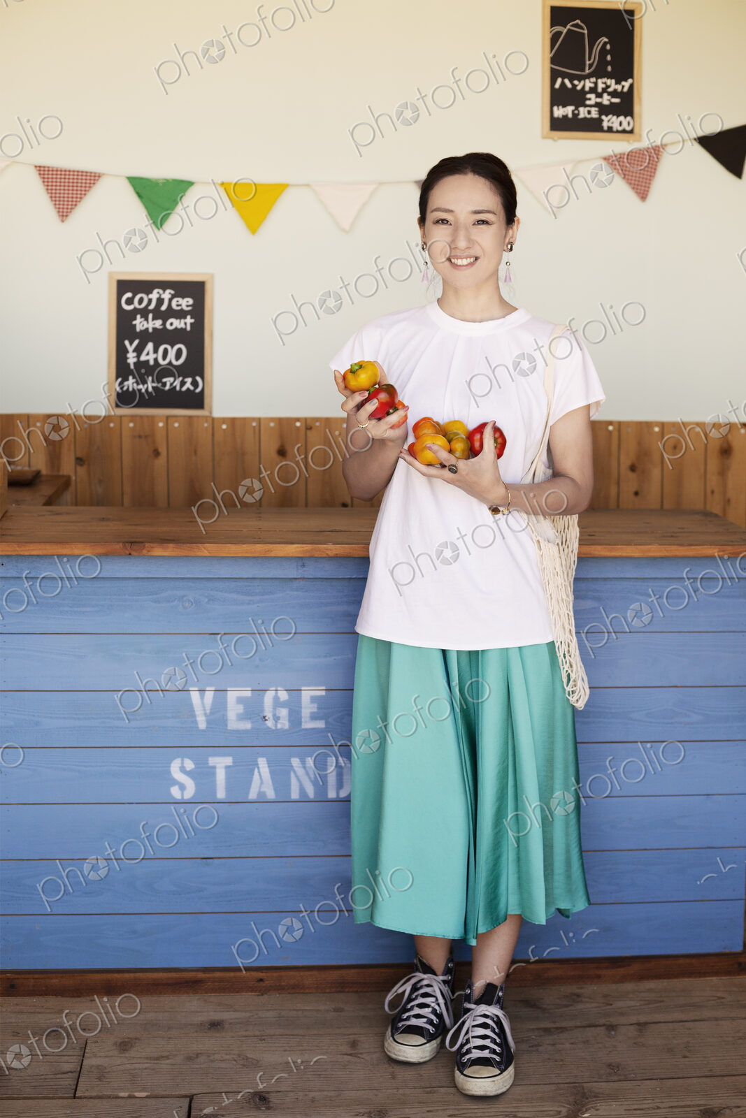 Japanese woman standing in a farm shop, holding vegetables, smiling at camera.