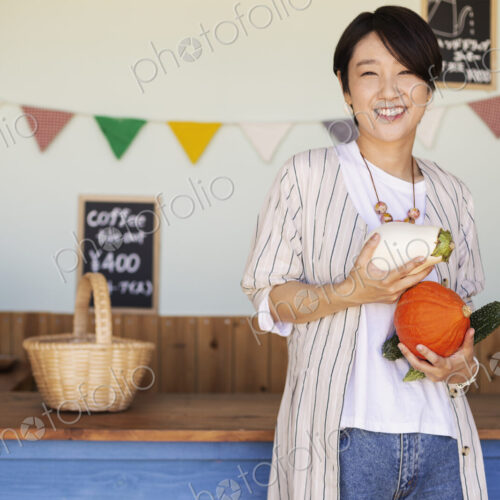 Japanese woman standing in a farm shop, holding vegetables, smiling at camera. Japanese woman standing in a farm shop, holding vegetables, smiling at camera.