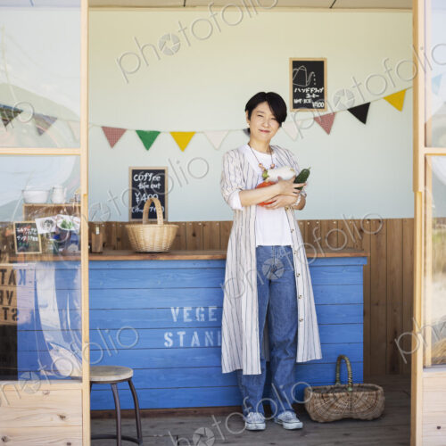 Japanese woman standing in a farm shop, holding vegetables, smiling at camera. Japanese woman standing in a farm shop, holding vegetables, smiling at camera.