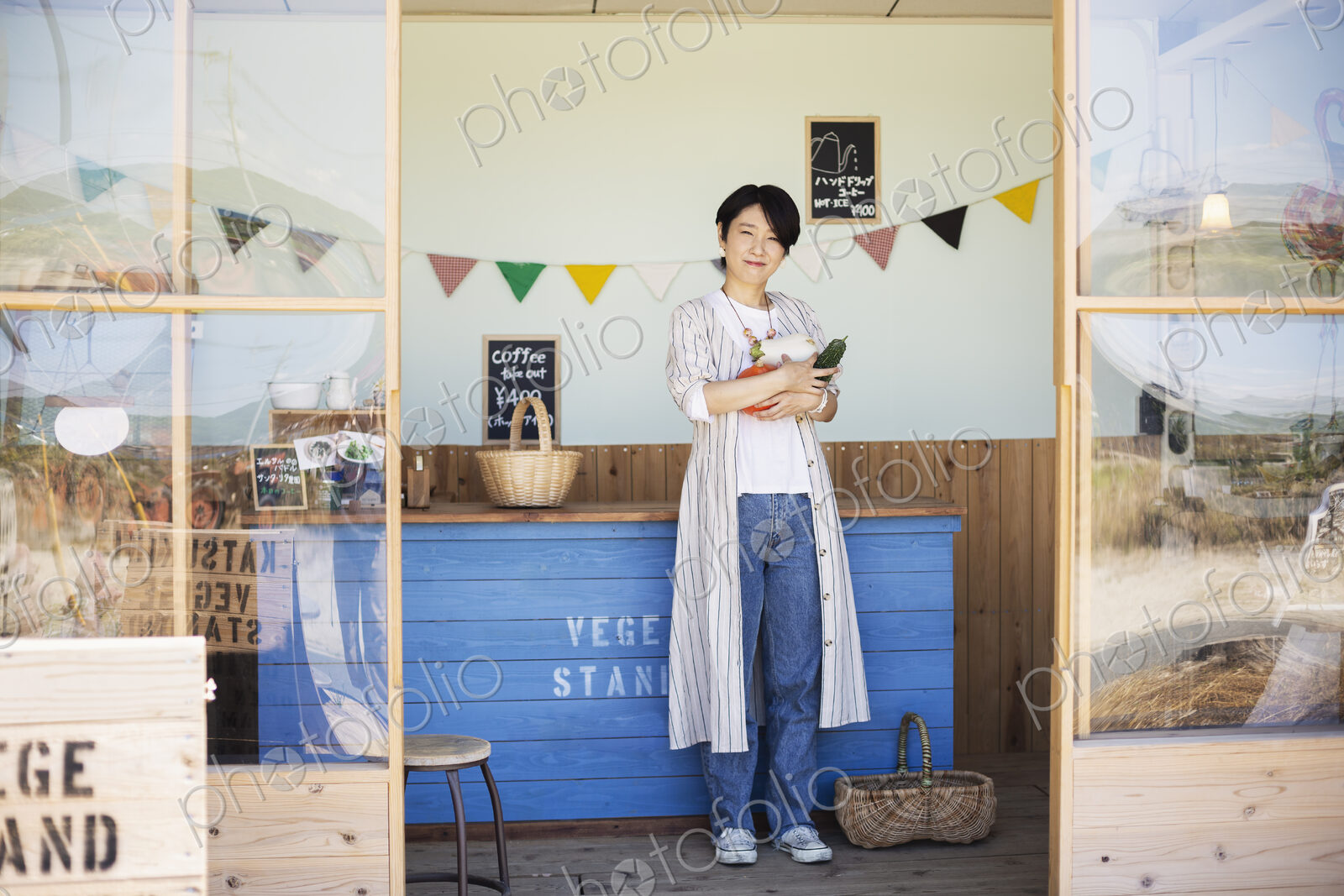 Japanese woman standing in a farm shop, holding vegetables, smiling at camera.