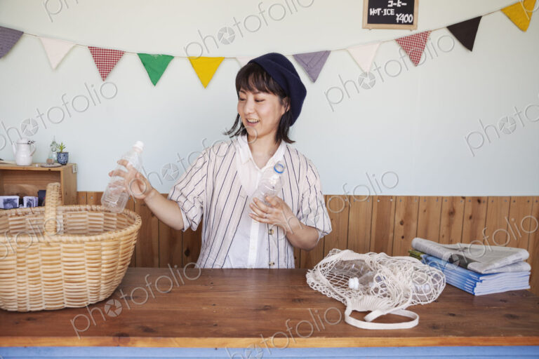 Japanese woman standing in a farm shop, sorting clear plastic bottles into basket.
