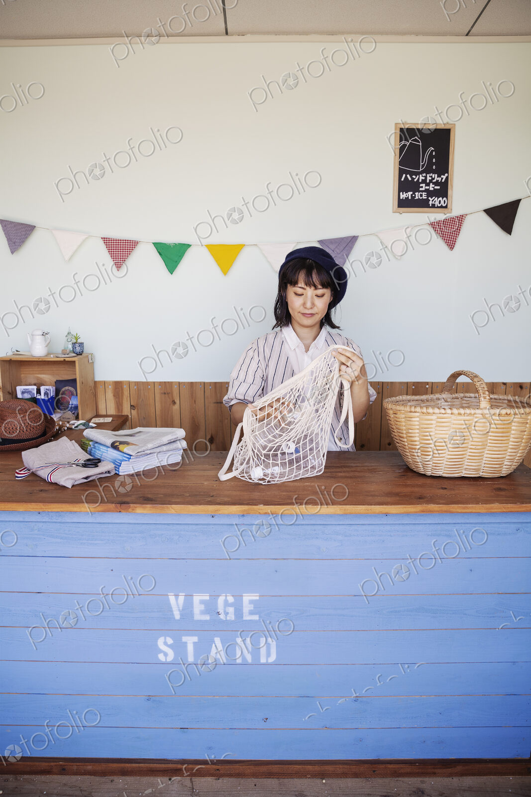 Japanese woman standing in a farm shop, sorting clear plastic bottles into net bag and…