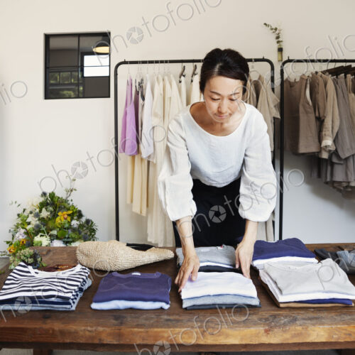 Japanese woman standing in a small fashion boutique, arranging T-Shirts on a coffee table. Japanese woman standing in a small fashion boutique, arranging T-Shirts on a coffee table.