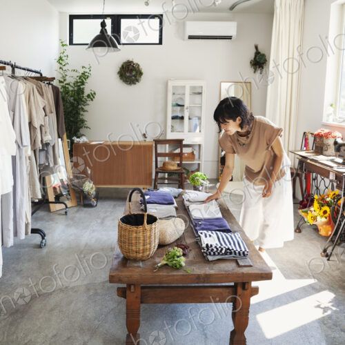 Japanese woman standing in a small fashion boutique, looking at T-Shirts on a coffee… Japanese woman standing in a small fashion boutique, looking at T-Shirts on a coffee…