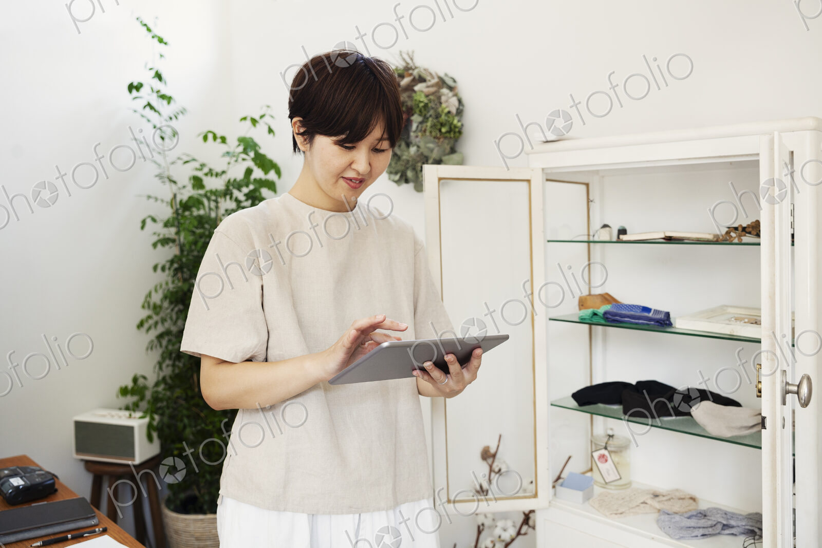 Japanese woman standing in a small fashion boutique, looking at digital tablet.