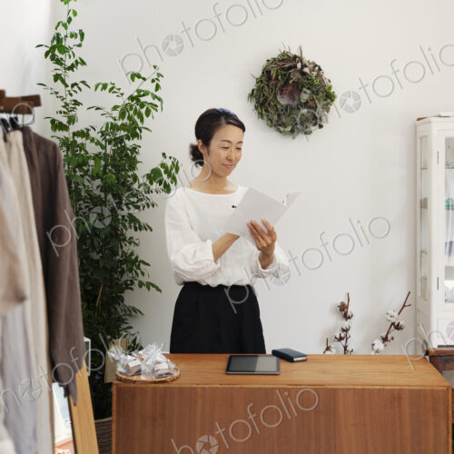 Japanese woman standing in a small fashion boutique, reading brochure. Japanese woman standing in a small fashion boutique, reading brochure.