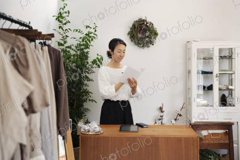 Japanese woman standing in a small fashion boutique, reading brochure.