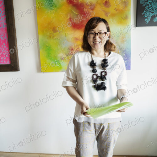 Japanese woman standing in front of abstract painting in an art gallery, smiling at…