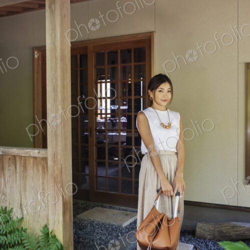 Japanese woman standing on a porch, holding handbag.