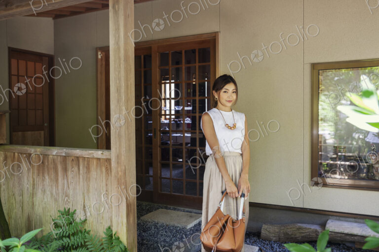 Japanese woman standing on a porch, holding handbag.