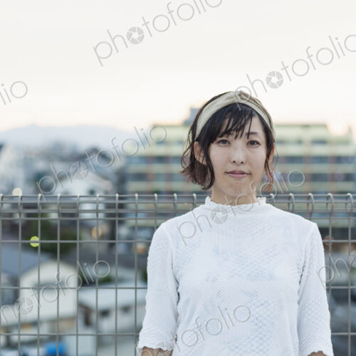 Japanese woman standing on a rooftop in an urban setting, looking at camera.