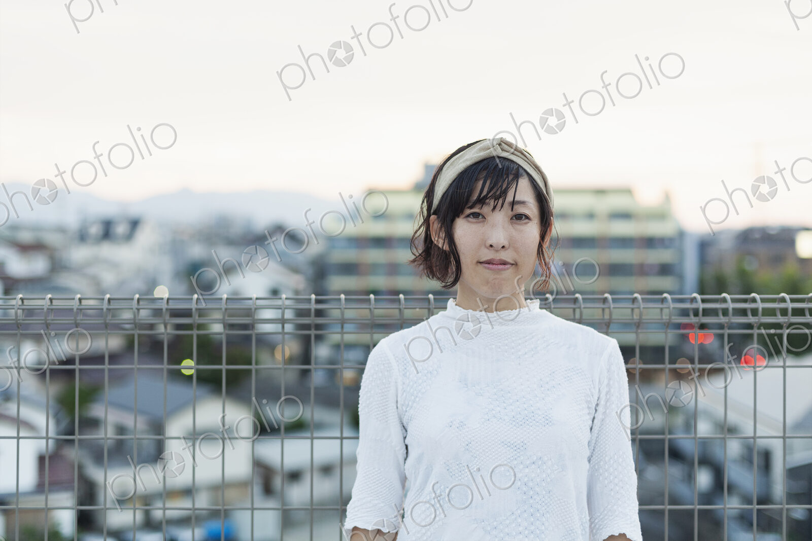 Japanese woman standing on a rooftop in an urban setting, looking at camera.