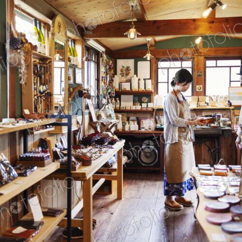 Japanese woman wearing apron standing in a leather shop, holding tan leather clutch… Japanese woman wearing apron standing in a leather shop, holding tan leather clutch…