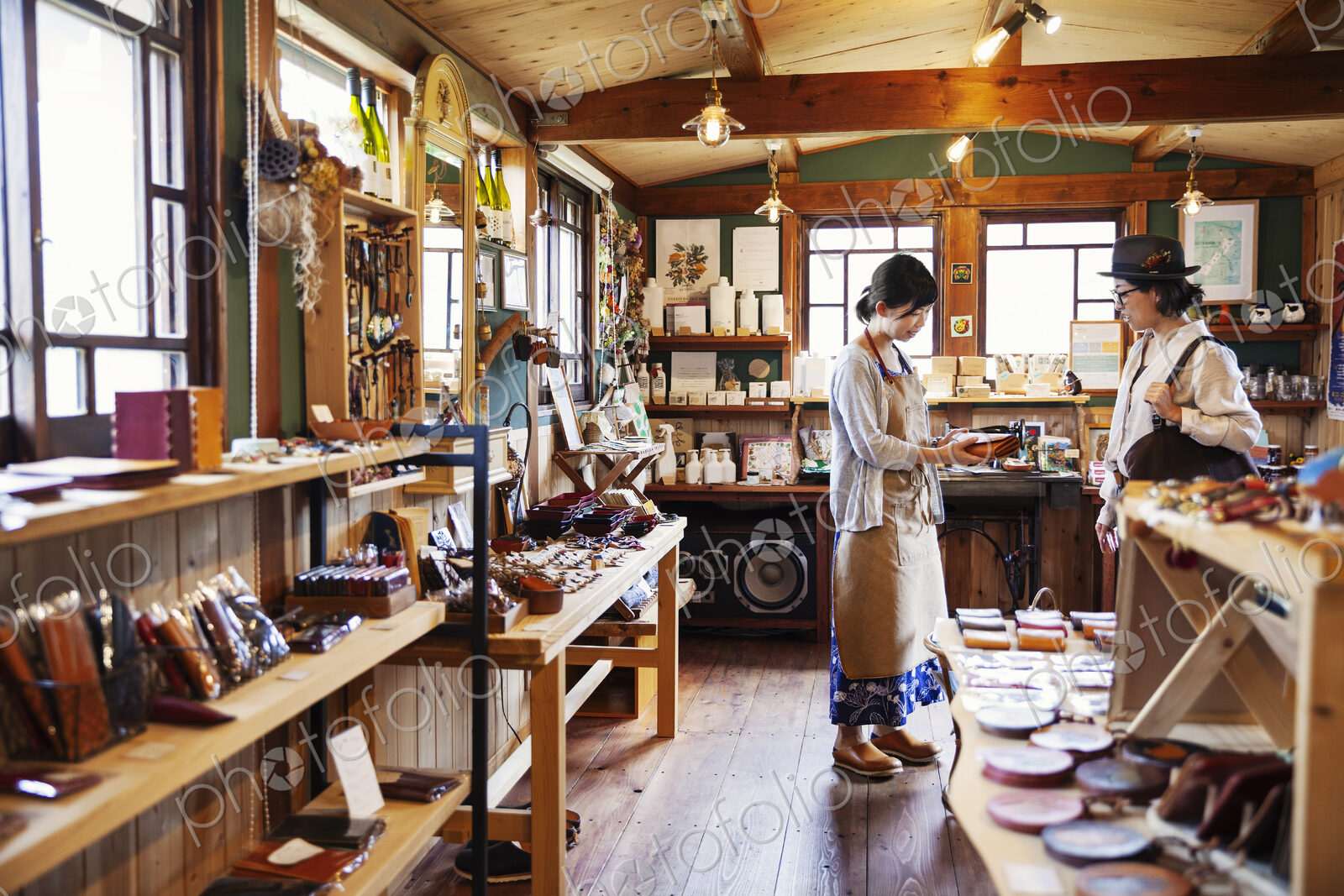 Japanese woman wearing apron standing in a leather shop, holding tan leather clutch…