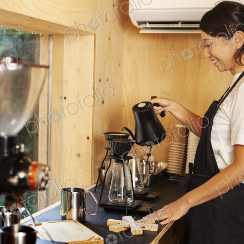 Japanese woman wearing apron standing in an Eco Cafe, preparing coffee. Japanese woman wearing apron standing in an Eco Cafe, preparing coffee.
