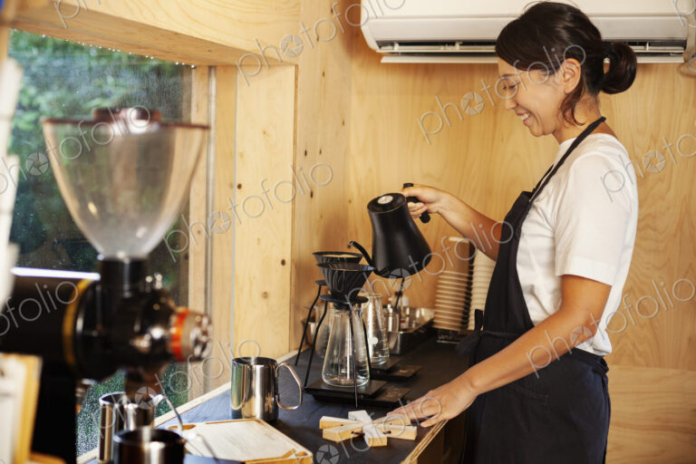 Japanese woman wearing apron standing in an Eco Cafe, preparing coffee.