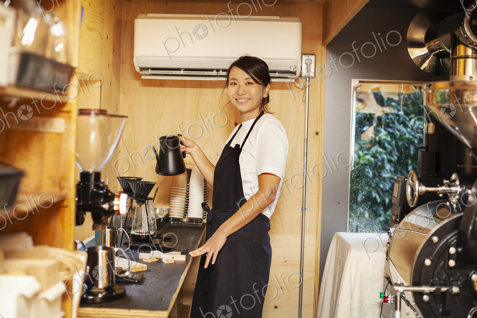 Japanese woman wearing apron standing in an Eco Cafe, preparing coffee, smiling at camera.