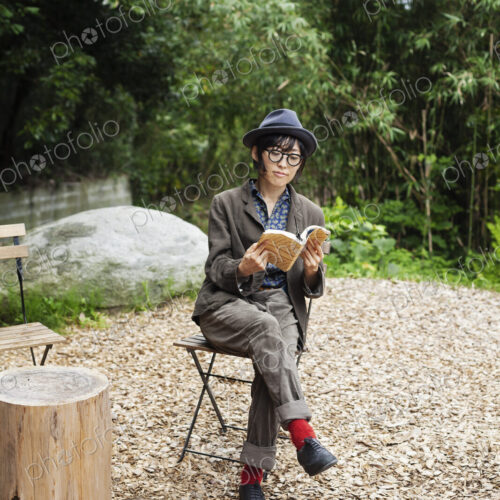Japanese woman wearing glasses and hat sitting on chair outside Eco Cafe, reading book. Japanese woman wearing glasses and hat sitting on chair outside Eco Cafe, reading book.