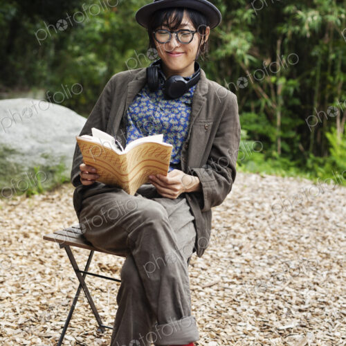 Japanese woman wearing glasses and hat sitting on chair outside Eco Cafe, reading book. Japanese woman wearing glasses and hat sitting on chair outside Eco Cafe, reading book.