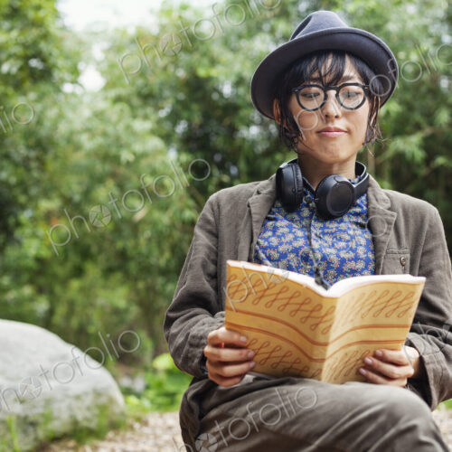Japanese woman wearing glasses and hat sitting on chair outside Eco Cafe, reading book. Japanese woman wearing glasses and hat sitting on chair outside Eco Cafe, reading book.