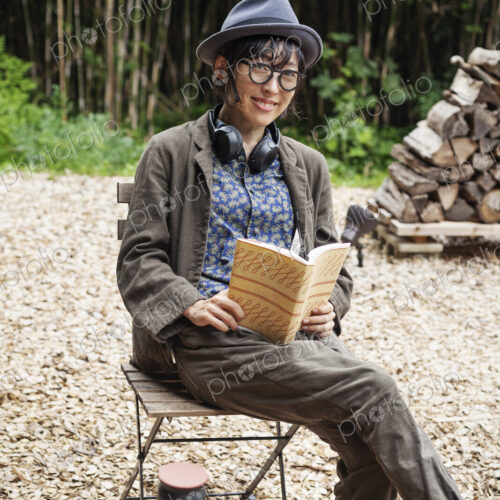 Japanese woman wearing glasses and hat sitting on chair outside Eco Cafe, reading book. Japanese woman wearing glasses and hat sitting on chair outside Eco Cafe, reading book.