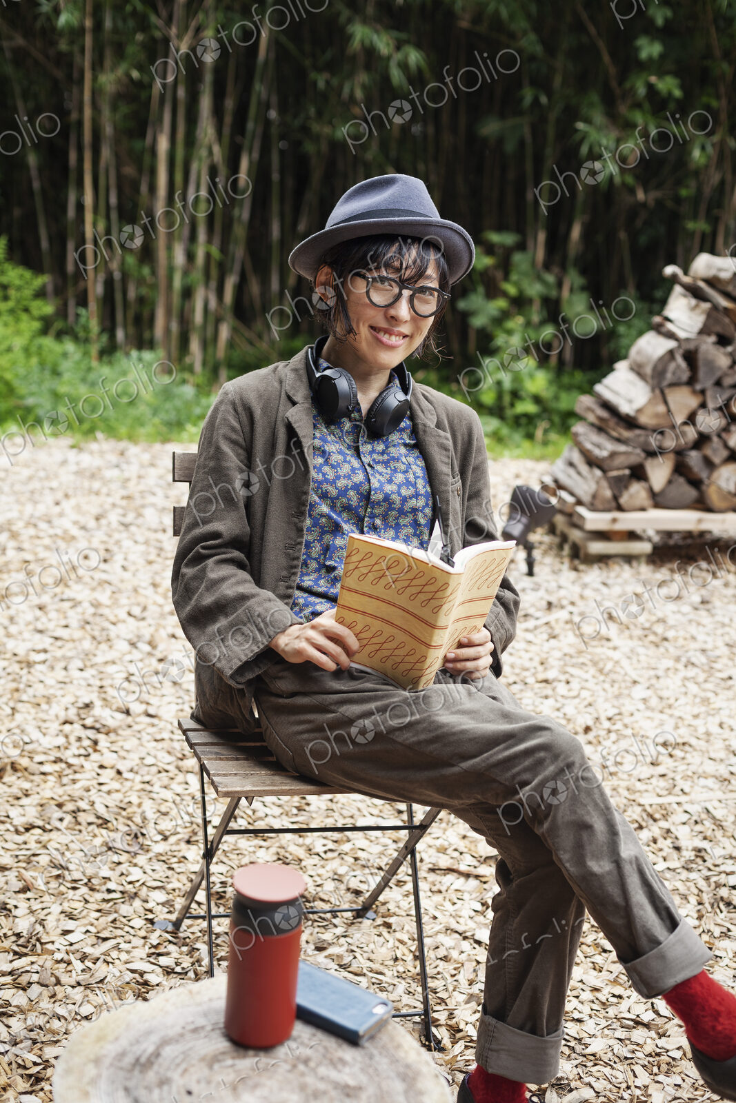 Japanese woman wearing glasses and hat sitting on chair outside Eco Cafe, reading book.