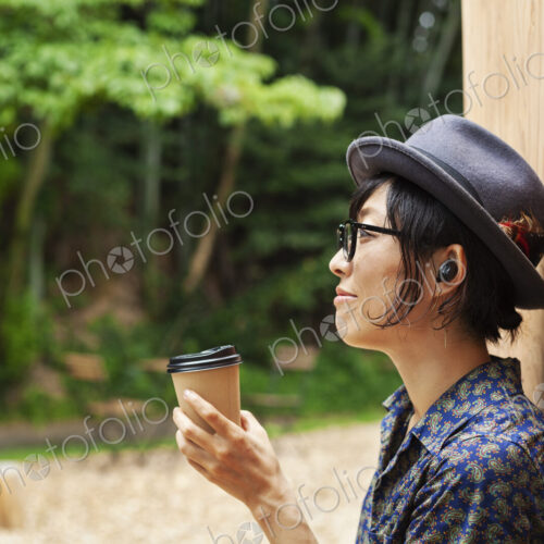 Japanese woman wearing glasses and hat standing outside Eco Cafe, holding paper cup.