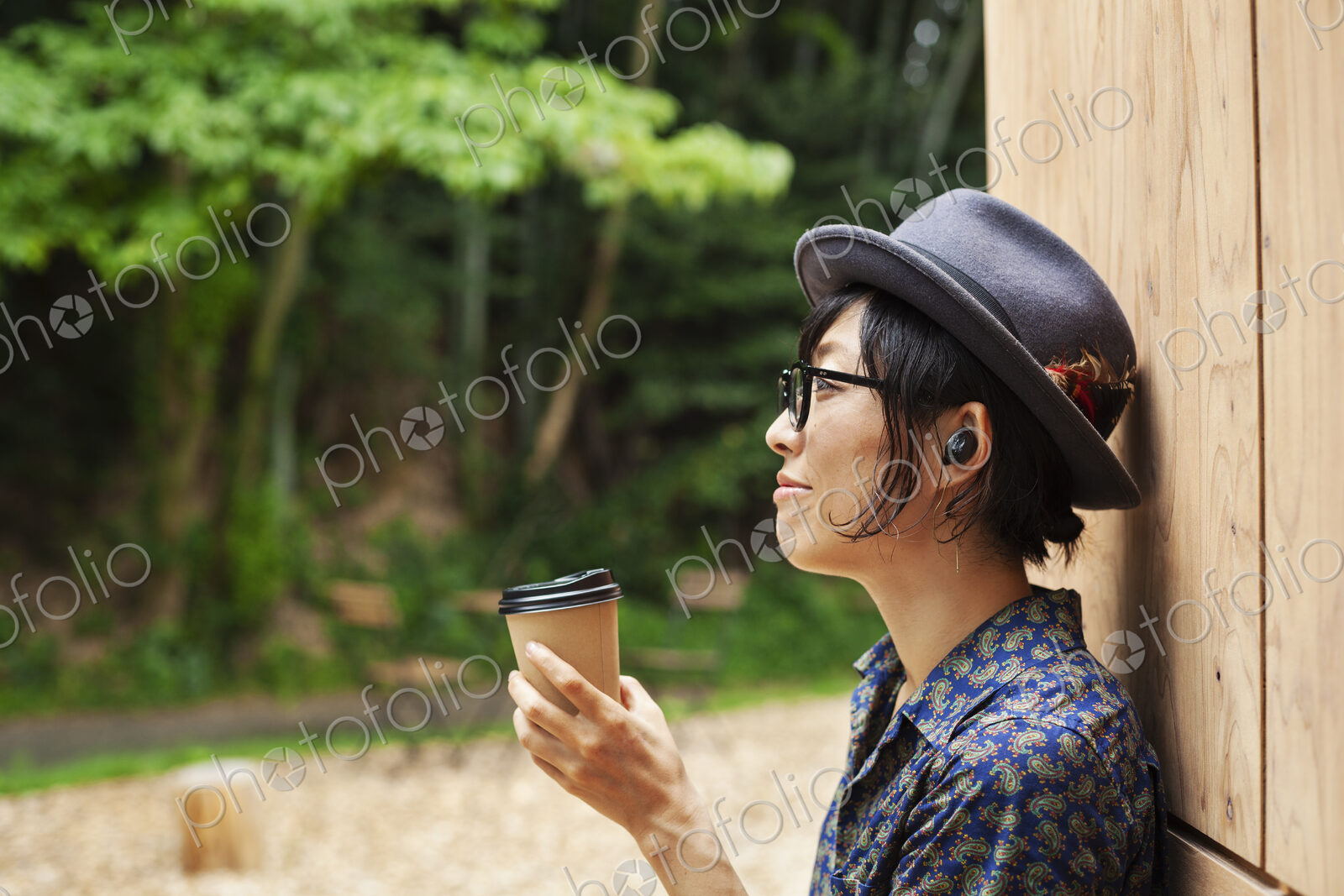 Japanese woman wearing glasses and hat standing outside Eco Cafe, holding paper cup.