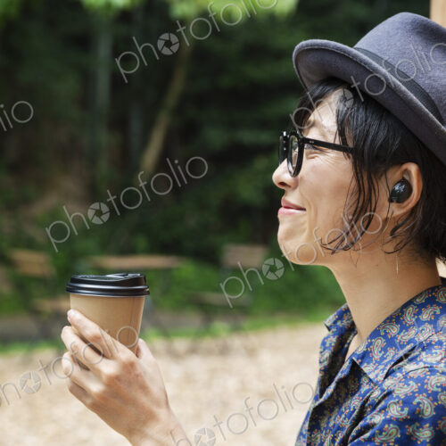 Japanese woman wearing glasses and hat standing outside Eco Cafe, holding paper cup.