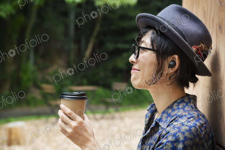 Japanese woman wearing glasses and hat standing outside Eco Cafe, holding paper cup.