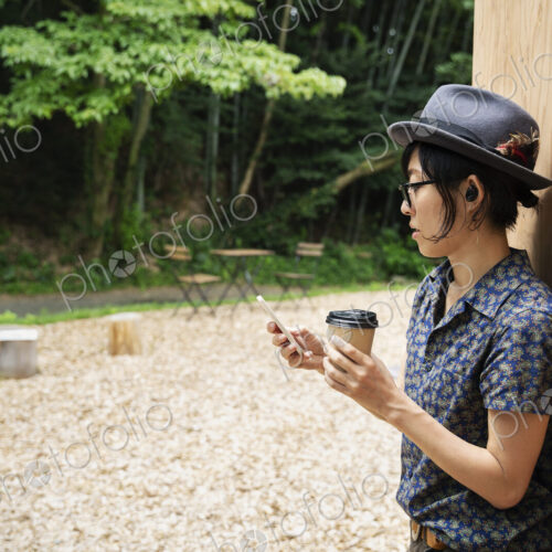 Japanese woman wearing glasses and hat standing outside Eco Cafe, holding paper cup.