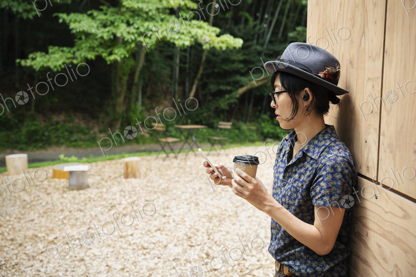 Japanese woman wearing glasses and hat standing outside Eco Cafe, holding paper cup.