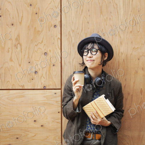 Japanese woman wearing glasses and hat standing outside Eco Cafe, holding paper cup…