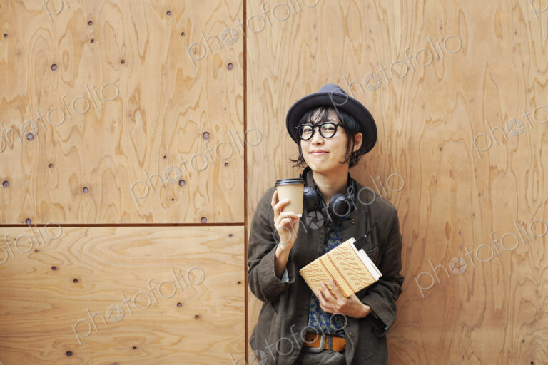 Japanese woman wearing glasses and hat standing outside Eco Cafe, holding paper cup…