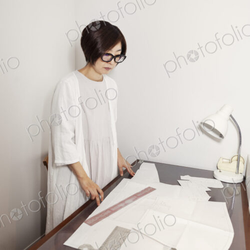 Japanese woman wearing glasses working at a desk in a small fashion boutique.