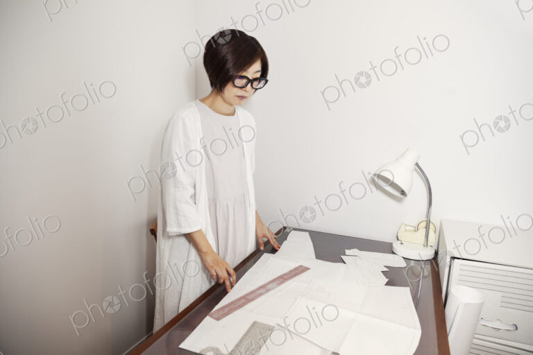 Japanese woman wearing glasses working at a desk in a small fashion boutique.
