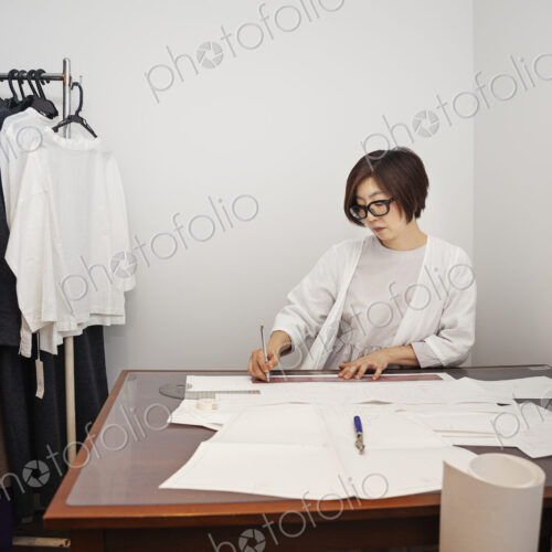 Japanese woman wearing glasses working at a desk in a small fashion boutique. Japanese woman wearing glasses working at a desk in a small fashion boutique.