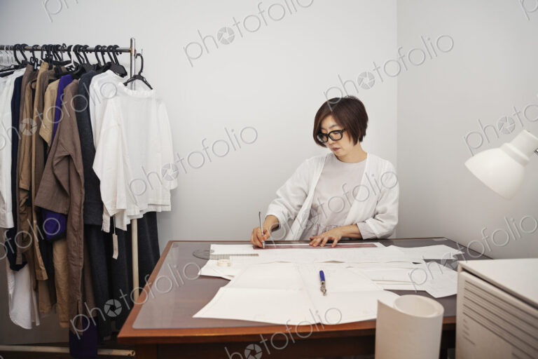 Japanese woman wearing glasses working at a desk in a small fashion boutique.