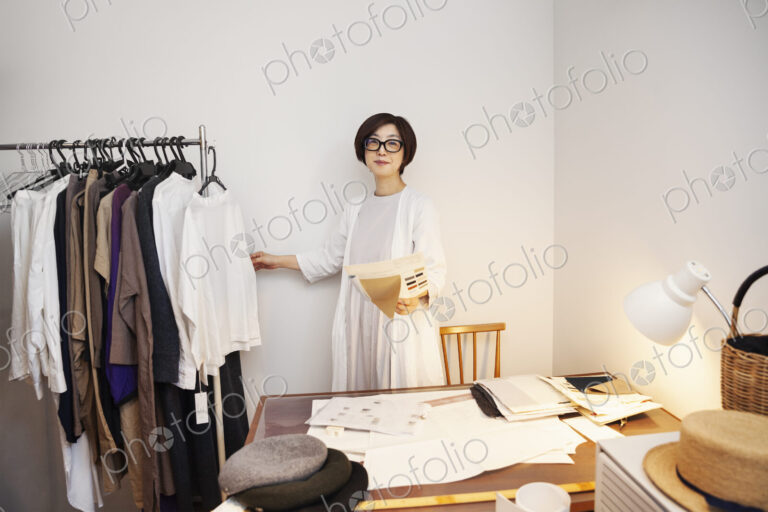 Japanese woman wearing glasses working at a desk in a small fashion boutique.