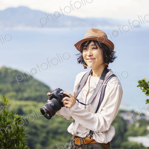 Japanese woman wearing hat and carrying backpack and camera standing on a cliff, ocean… Japanese woman wearing hat and carrying backpack and camera standing on a cliff, ocean…