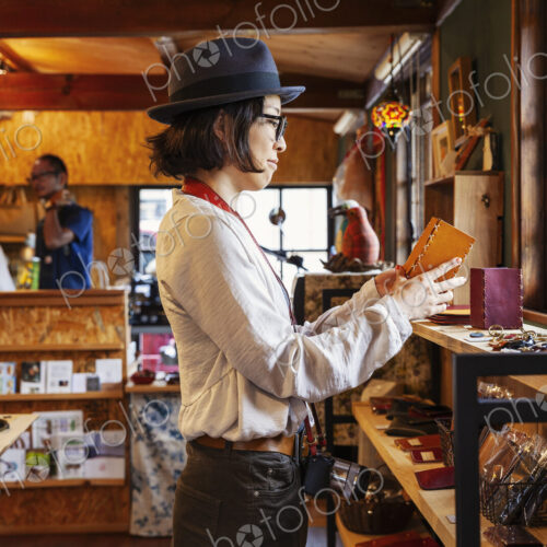 Japanese woman wearing hat and glasses browsing merchandise in a leather shop. Japanese woman wearing hat and glasses browsing merchandise in a leather shop.