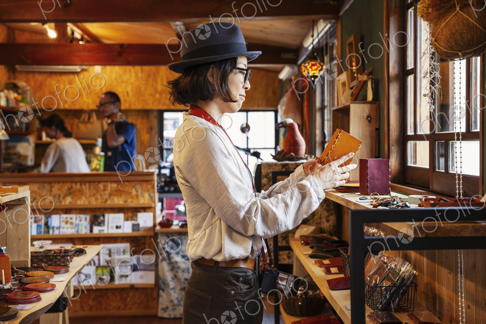Japanese woman wearing hat and glasses browsing merchandise in a leather shop.