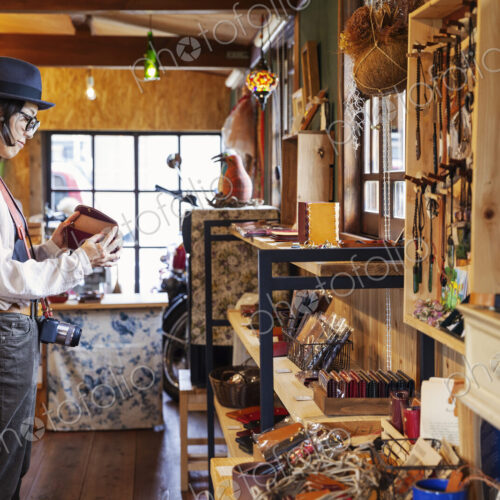Japanese woman wearing hat and glasses browsing merchandise in a leather shop. Japanese woman wearing hat and glasses browsing merchandise in a leather shop.