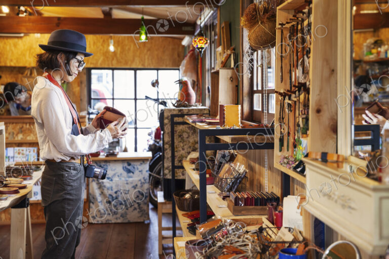 Japanese woman wearing hat and glasses browsing merchandise in a leather shop.