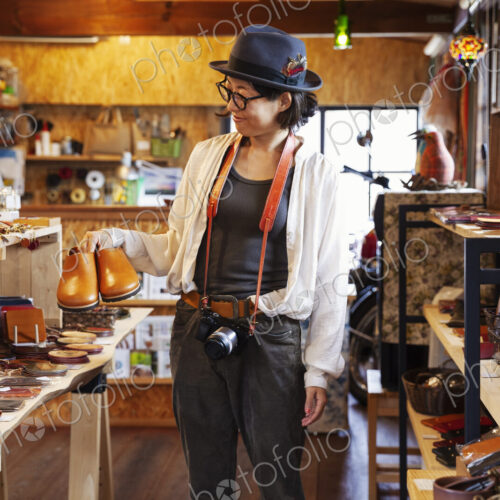 Japanese woman wearing hat and glasses browsing merchandise in a leather shop. Japanese woman wearing hat and glasses browsing merchandise in a leather shop.