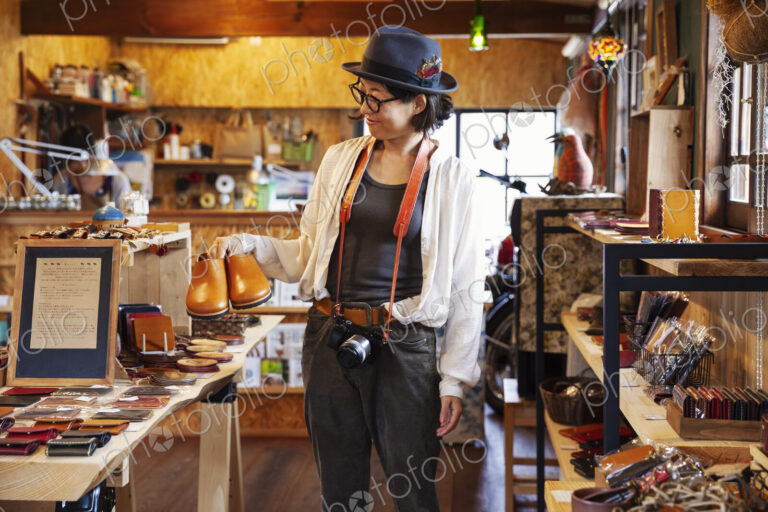 Japanese woman wearing hat and glasses browsing merchandise in a leather shop.