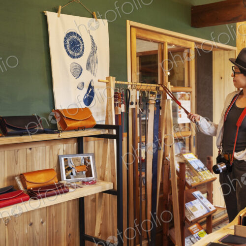 Japanese woman wearing hat and glasses browsing merchandise in a leather shop. Japanese woman wearing hat and glasses browsing merchandise in a leather shop.