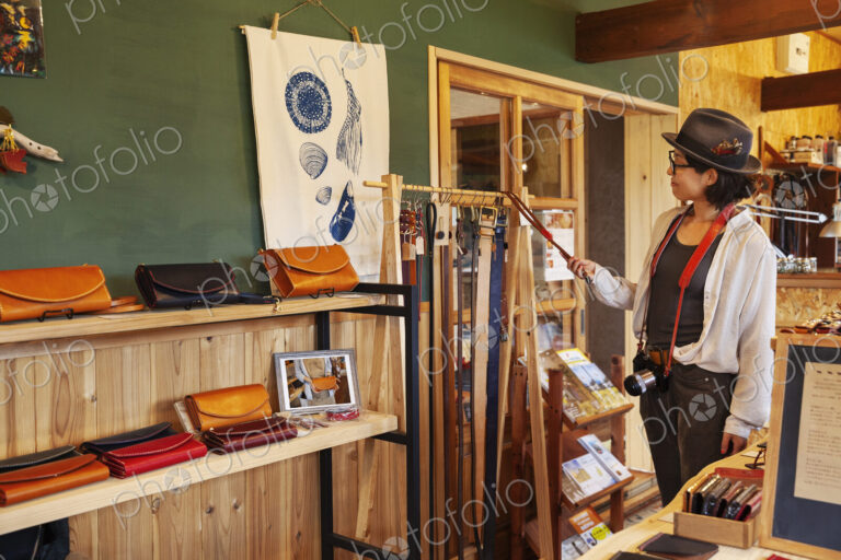 Japanese woman wearing hat and glasses browsing merchandise in a leather shop.