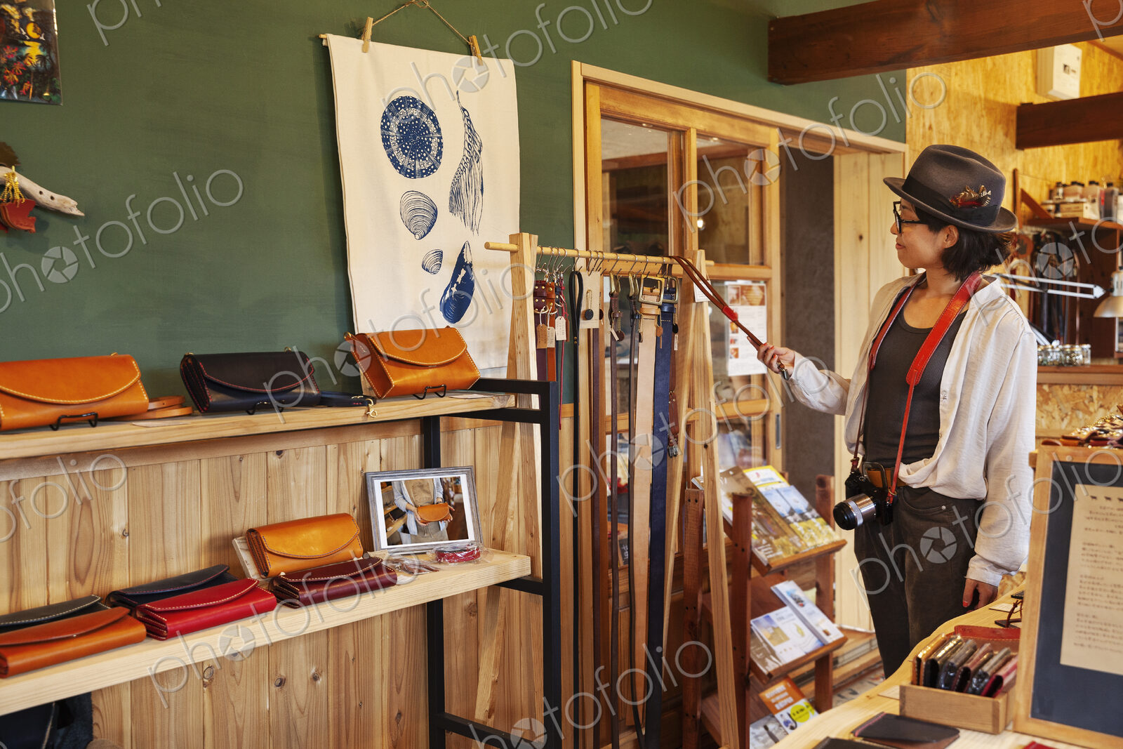 Japanese woman wearing hat and glasses browsing merchandise in a leather shop.