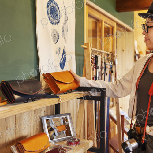 Japanese woman wearing hat and glasses browsing merchandise in a leather shop. Japanese woman wearing hat and glasses browsing merchandise in a leather shop.